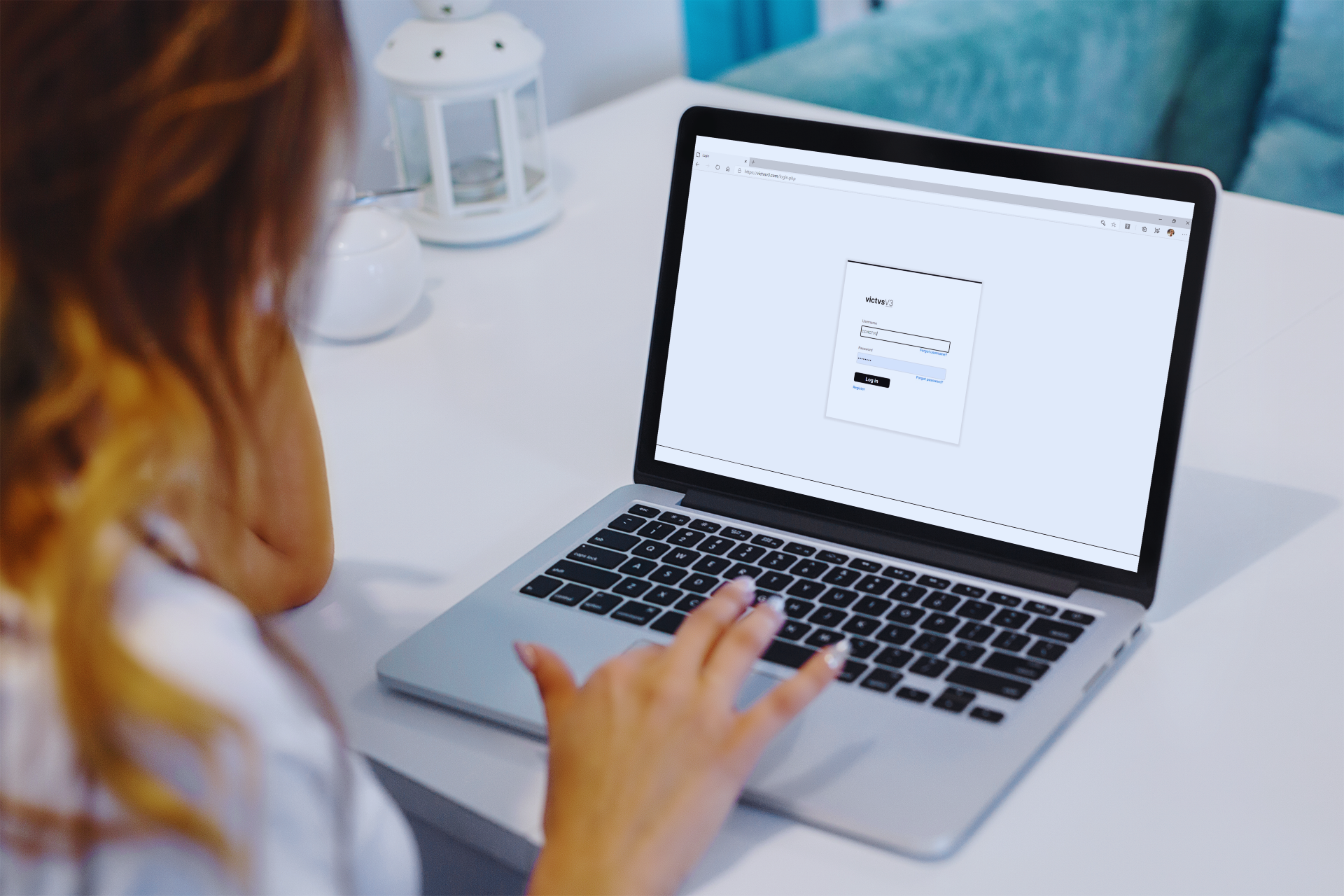 A woman sat working on a laptop with blonde hair, her back to the camera and out of focus. The computer screen shows a login screen.
