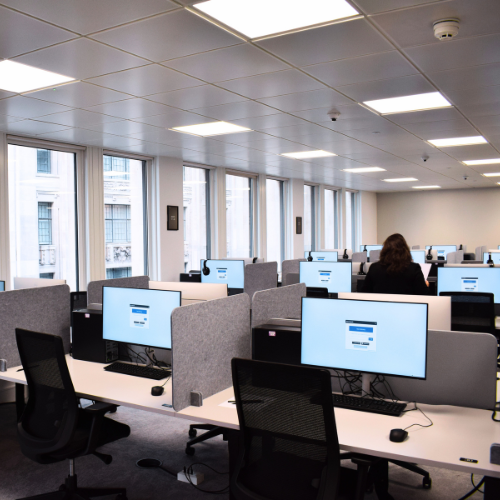 Photograph of test centre room filled with desks, a monitor on each desk.