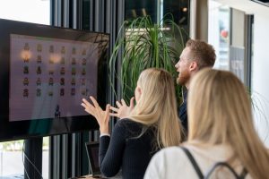 People look up at a screen, backs to camera, playing a game called Beat the Cheat