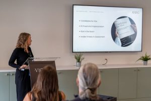 Niamh PIerce from ASRG stands in front of a lecturn and presentation screen, about to go through her research on Candidates for Hire.
